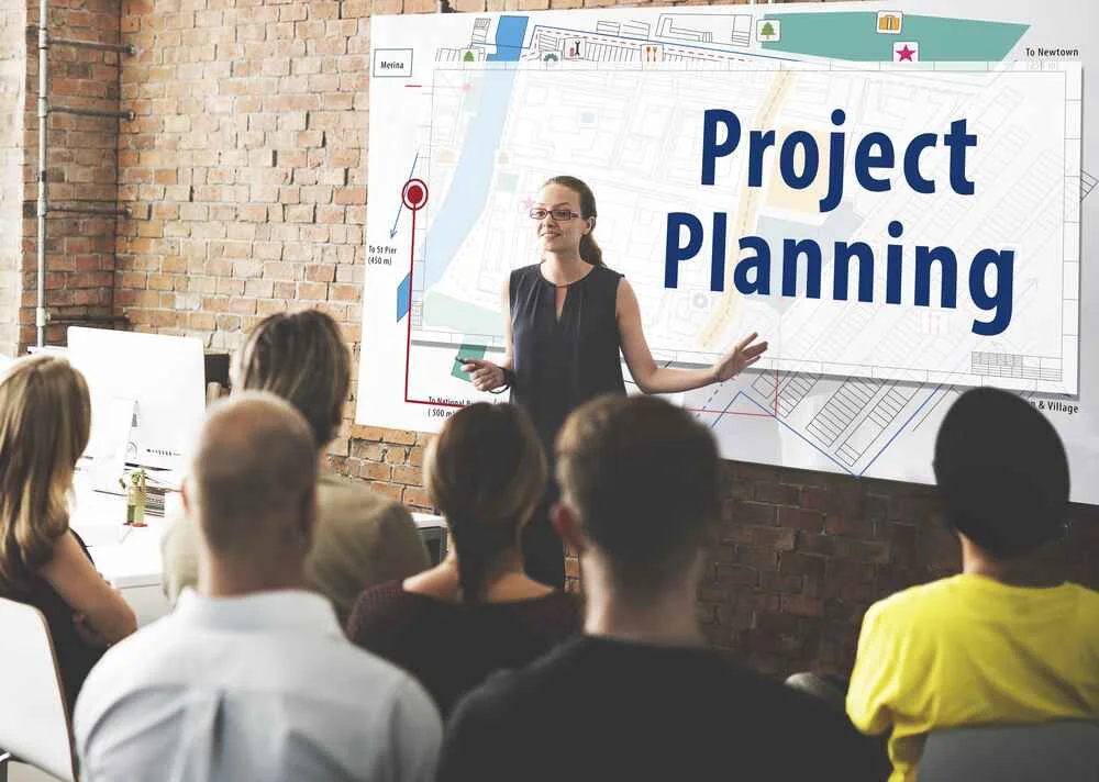 A presenter explaining project planning to a small team, showing a simple project management setup ideal for beginners