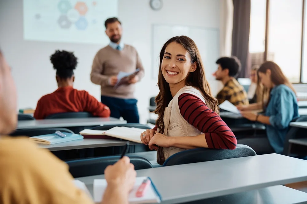 Smiling female student sitting in a classroom with other students and an instructor, representing engaging and worthwhile courses