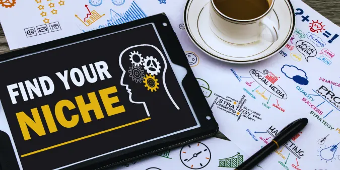 Find your niche concept displayed on a tablet with business strategy notes, coffee cup, and planning sketches for choosing a freelance writing niche.