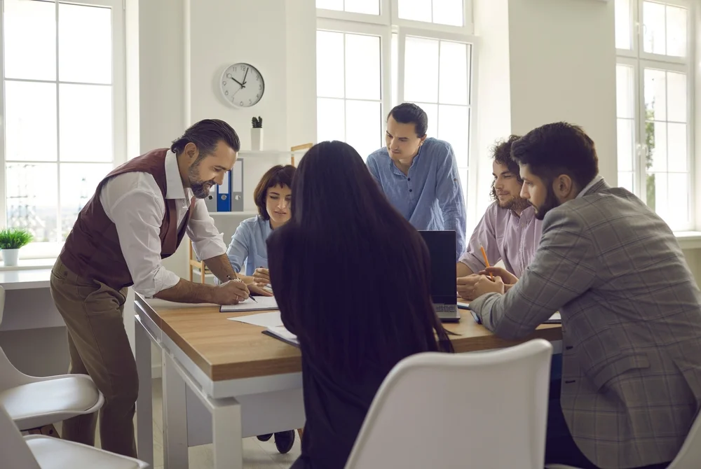 Group of professionals gathered around a table as an instructor explains concepts, illustrating the collaborative and expert-led learning experience of MasterClass