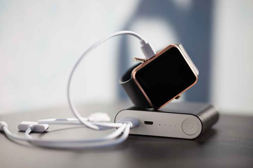 Affordable smartwatch charging on a power bank with USB cable, illustrating real-world battery life testing and manufacturer claim comparison for budget fitness smartwatches.