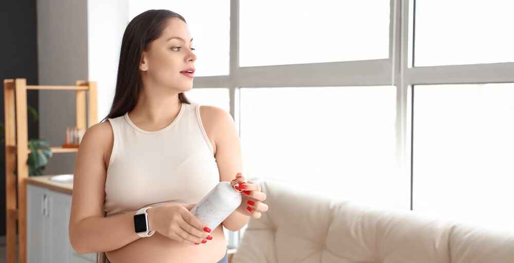 Woman wearing a budget fitness smartwatch while holding a water bottle at home, showcasing mid-range $50–$100 affordable fitness smartwatches for heart rate and workout tracking.